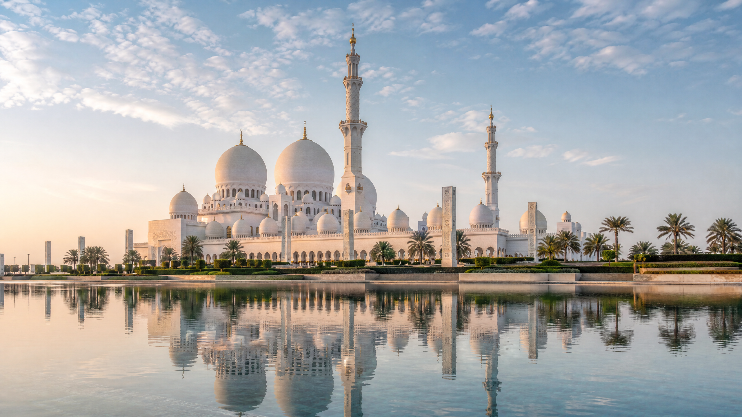 Panoramic view of Sheikh Zayed Grand Mosque in Abu Dhabi reflected in calm water at soft morning light.