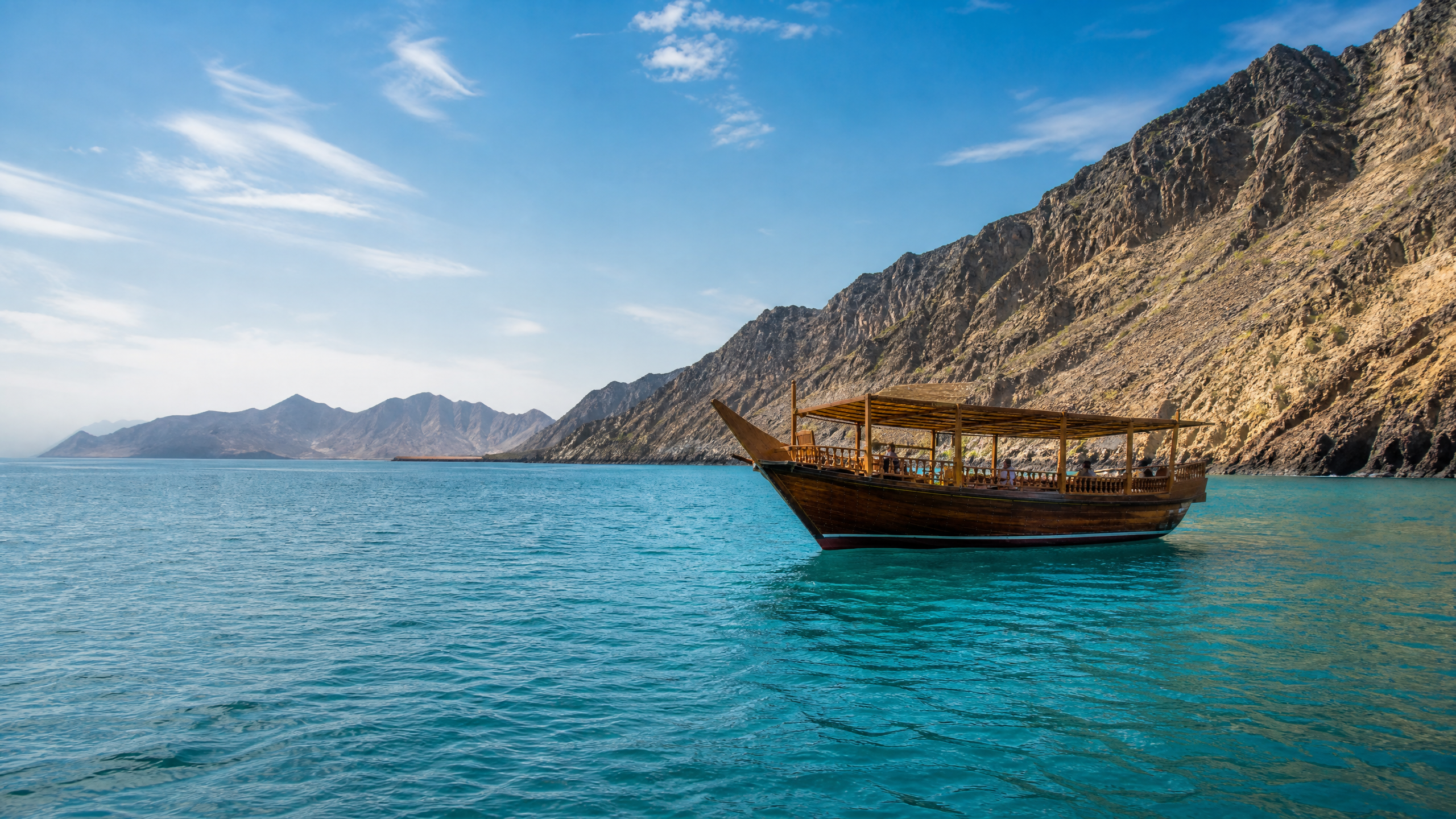 Traditional wooden dhow sailing on turquoise water beside the rocky Fujairah coastline
